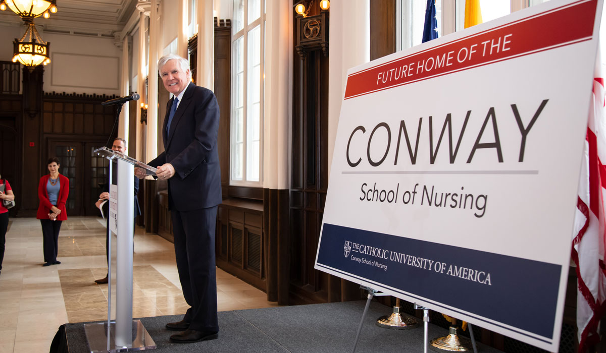 Bill Conway at a podium next to a poster with Conway School of Nursing written on it