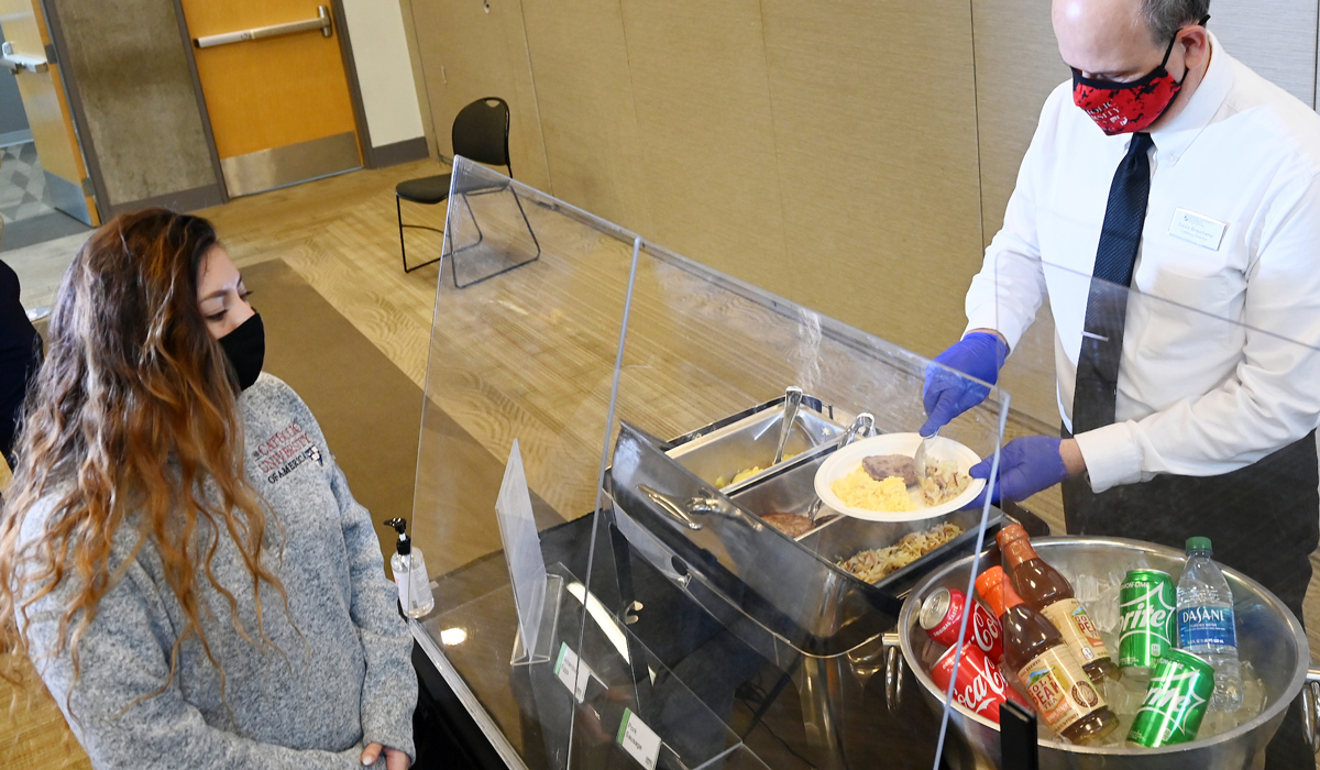 Contactless catering on campus shows server behind plexiglass shield