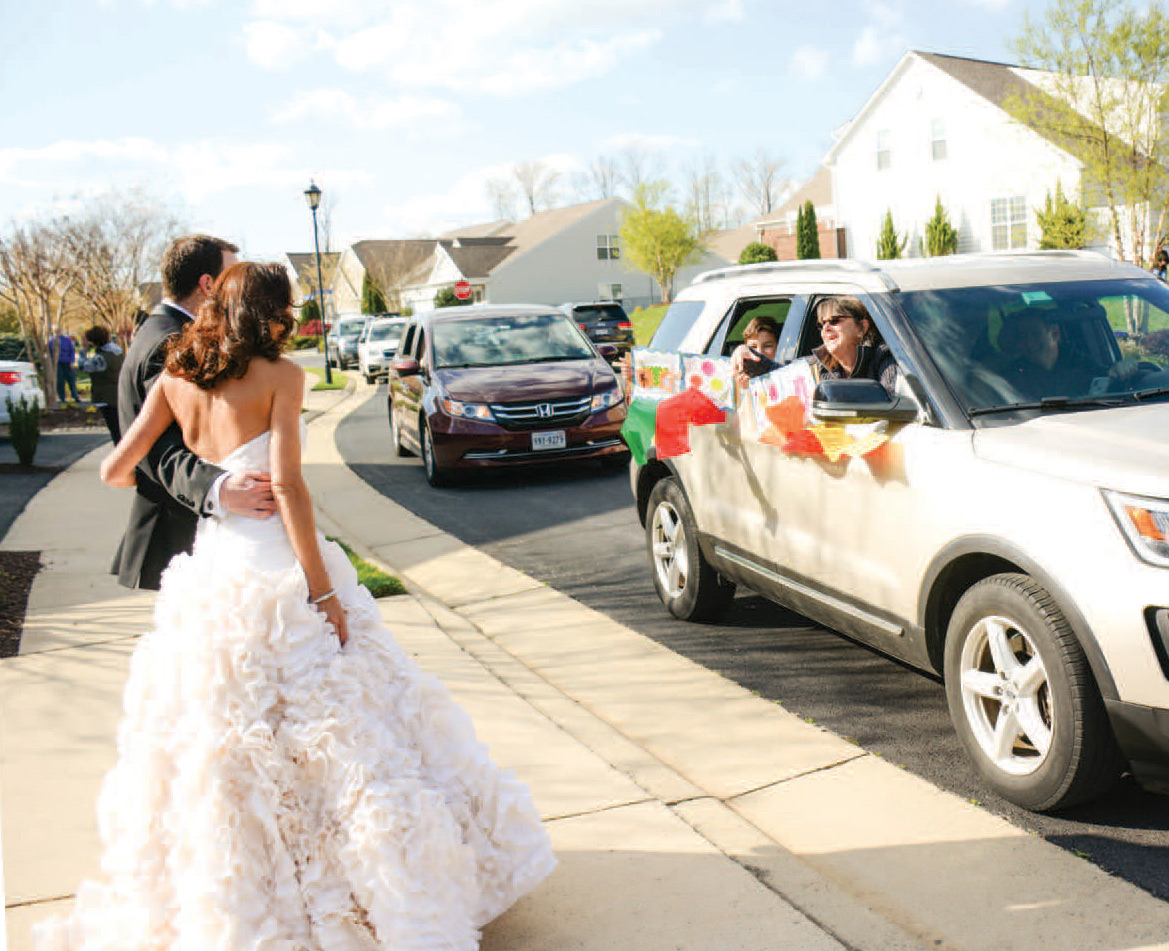 Newly married couple receives congratulations from friends and family as they drive by