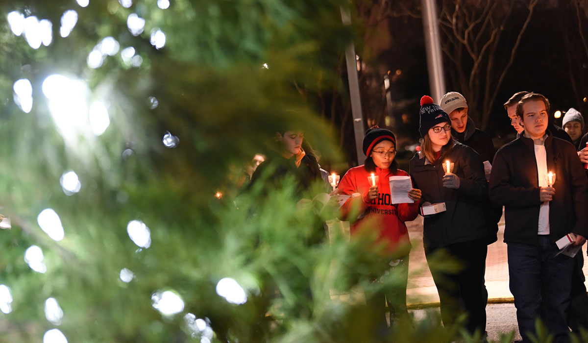 Students holding candles next to tree