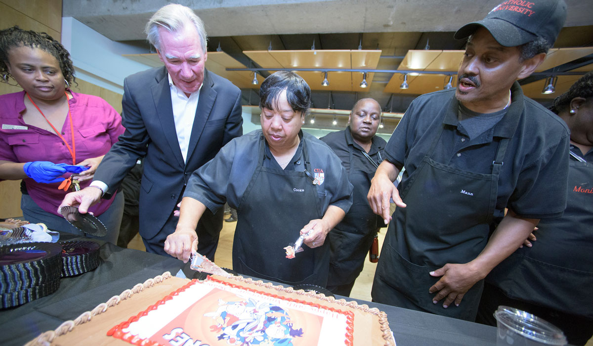Ms. Cookie cuts her cake, surrounded by colleagues