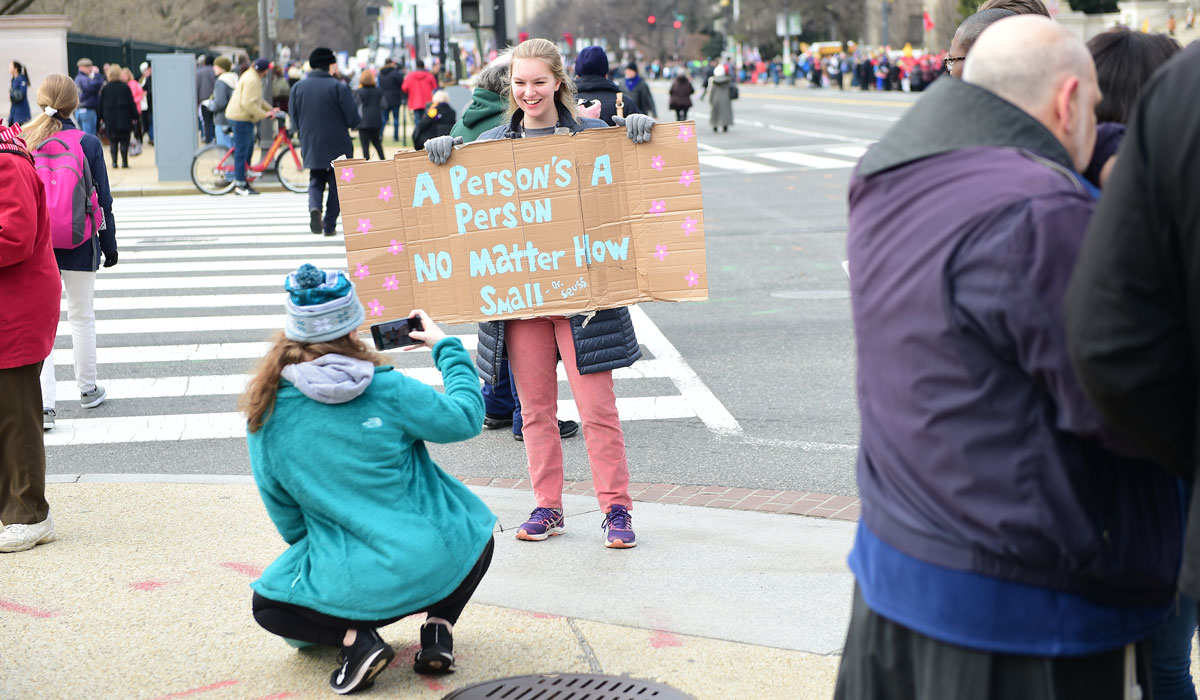 Female student taking picture of female friend with sign in downtown Washington, D.C.