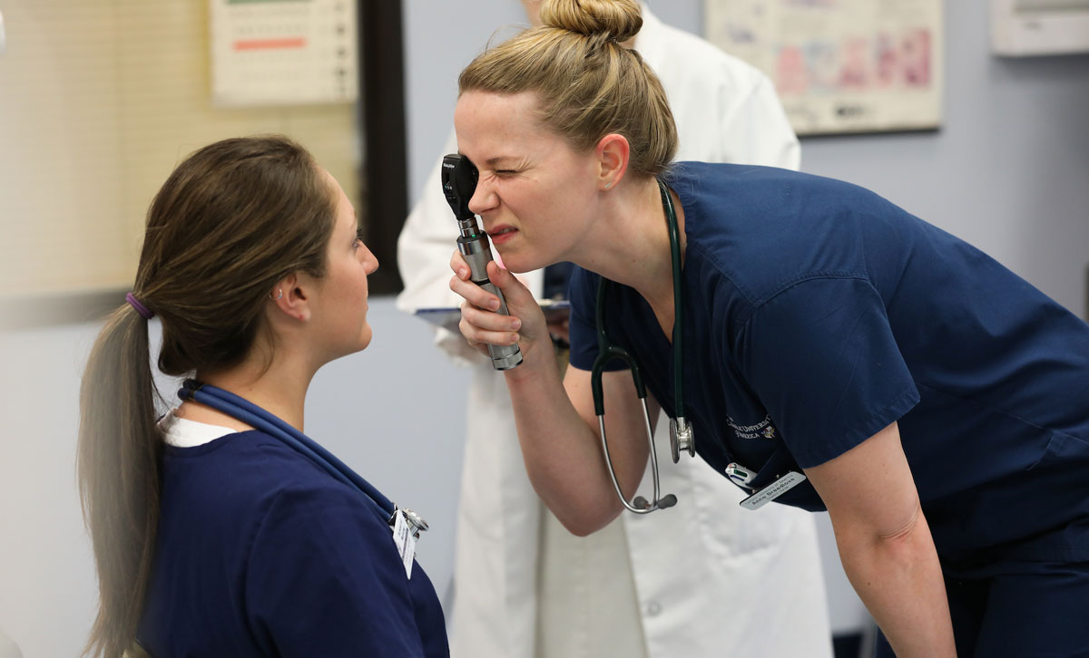 Nursing student examining another nursing student's eye