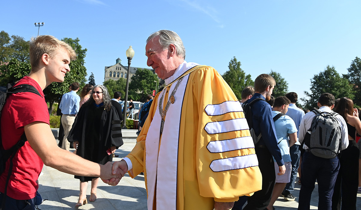 President Garvey shaking hands with a male student outside Basilica
