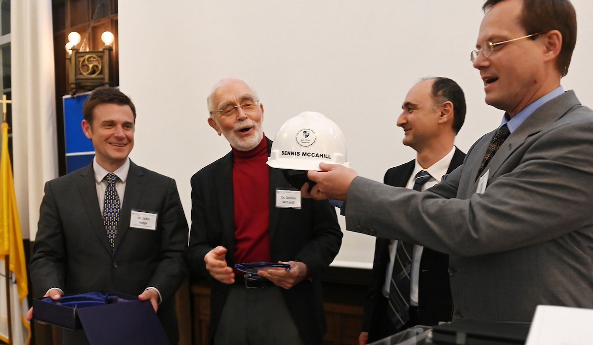 John Judge, dean of the School of Engineering; Dennis McCahill, founding director of CEM; Arash Massoudieh, professor and chair of civil engineering; and Gunnar Lucko, professor and director of CEM admire a construction hard hat with Dennis McCahill’s name on it. 