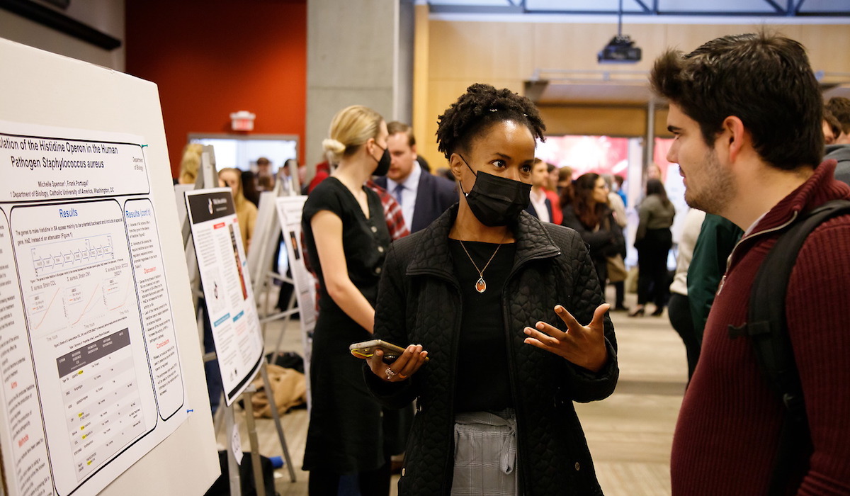 A student presents her research poster to another student at Research Day