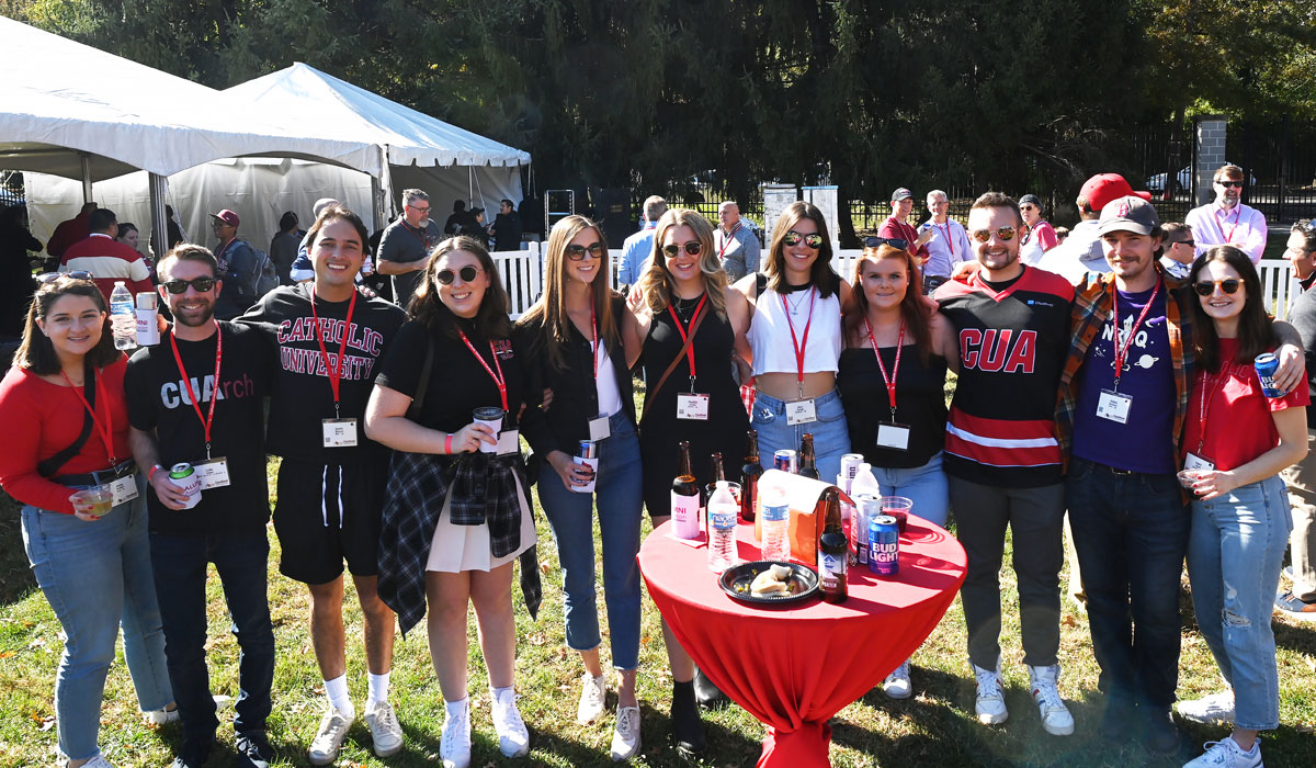 Alumni smile in CatholicU gear while they catch up over drinks from the tent reception