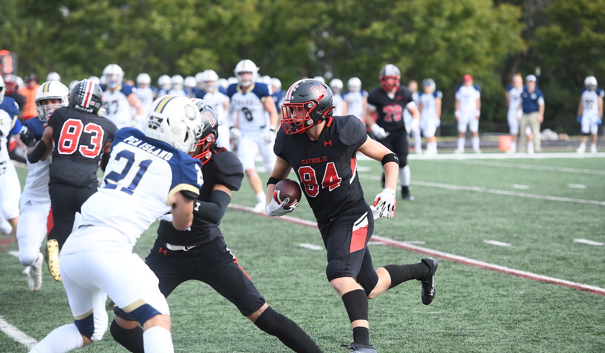 CatholicU football player running down the field, ball in hand, during a game against Coast Guard.