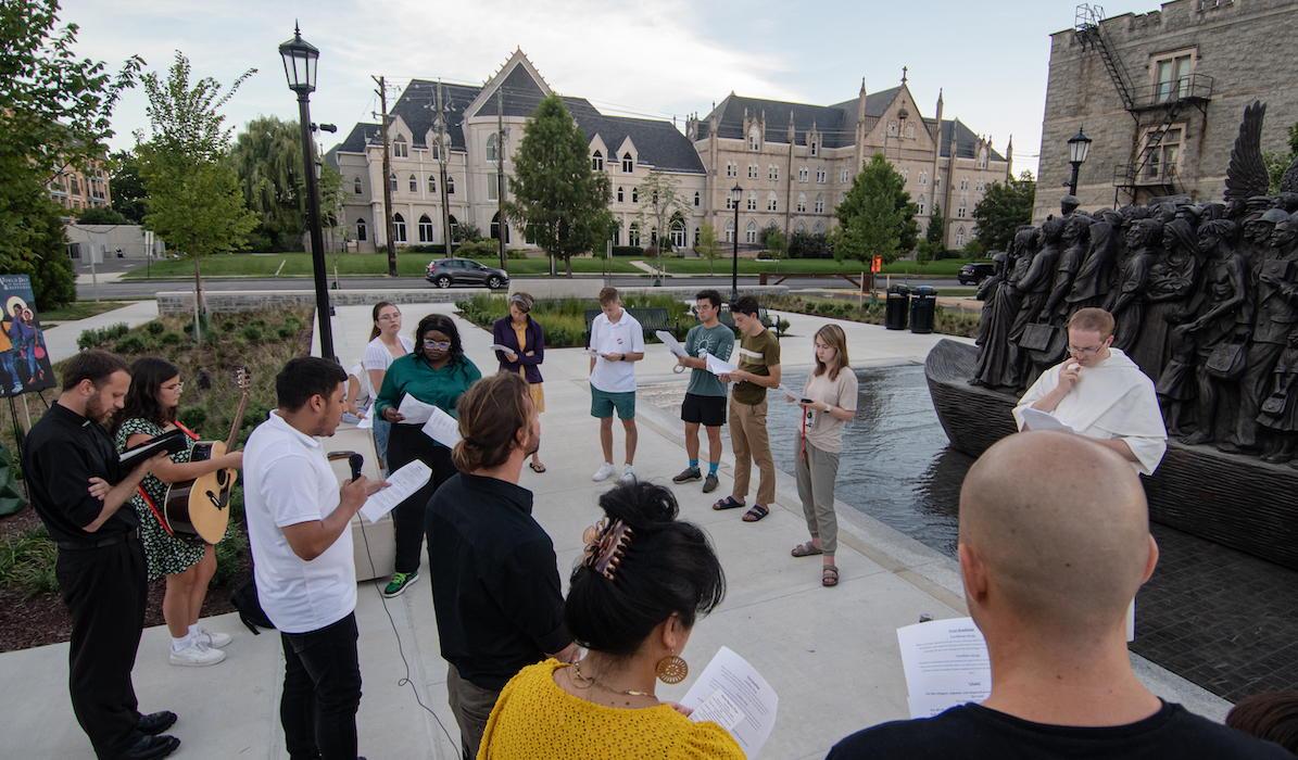 students and campus ministry staff pray at the angels unawares sculpture