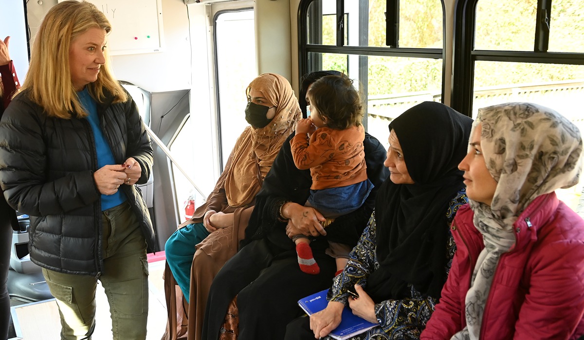 ate (Teeling) Talbot, B.A. 1990, director of operations and finance for Solutions in Hometown Connections, speaks with Afghan refugees during a Welcome Workshop program in a mobile classroom 