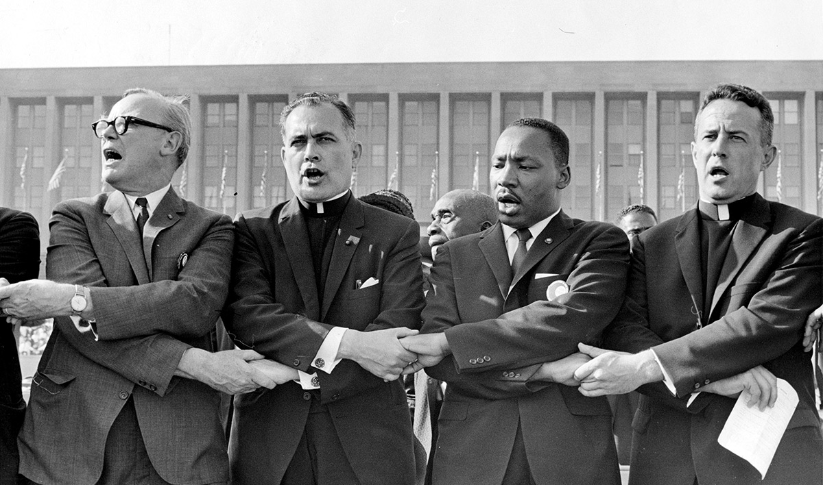 Catholic University alumnus Rev. Theodore M. Hesburgh, C.S.C. (second from left), former president of the University of Notre Dame, joins Martin Luther King Jr. in singing “We Shall Overcome” during a rally in support of the Civil Rights Act at Soldier Field in Chicago, 1964. 