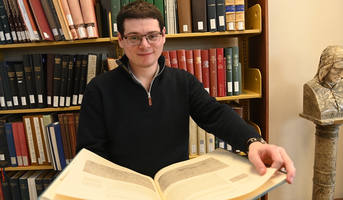 History doctoral candidate Amos Bronner is seen with a book of facsimiles of medieval documents at Mullen Library. (Catholic University/ Patrick G. Ryan)
