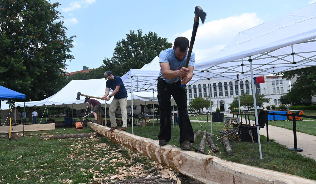 Team members use axes to shape a truss beam