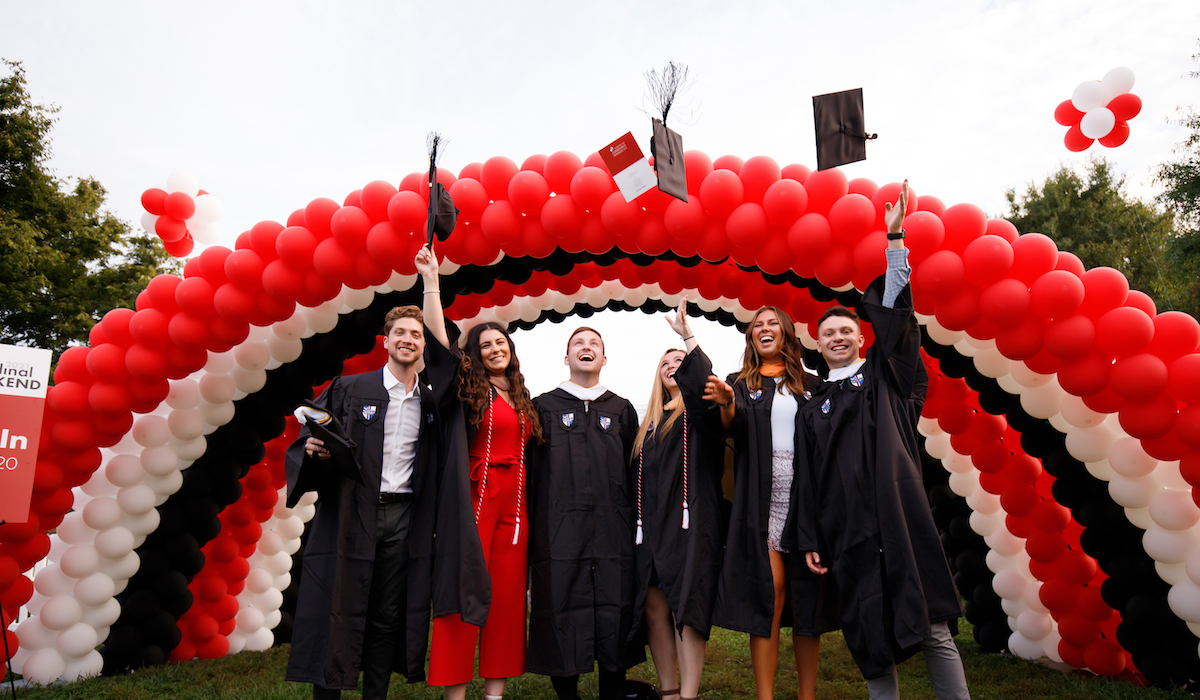 Graduates toss their caps under a balloon archway