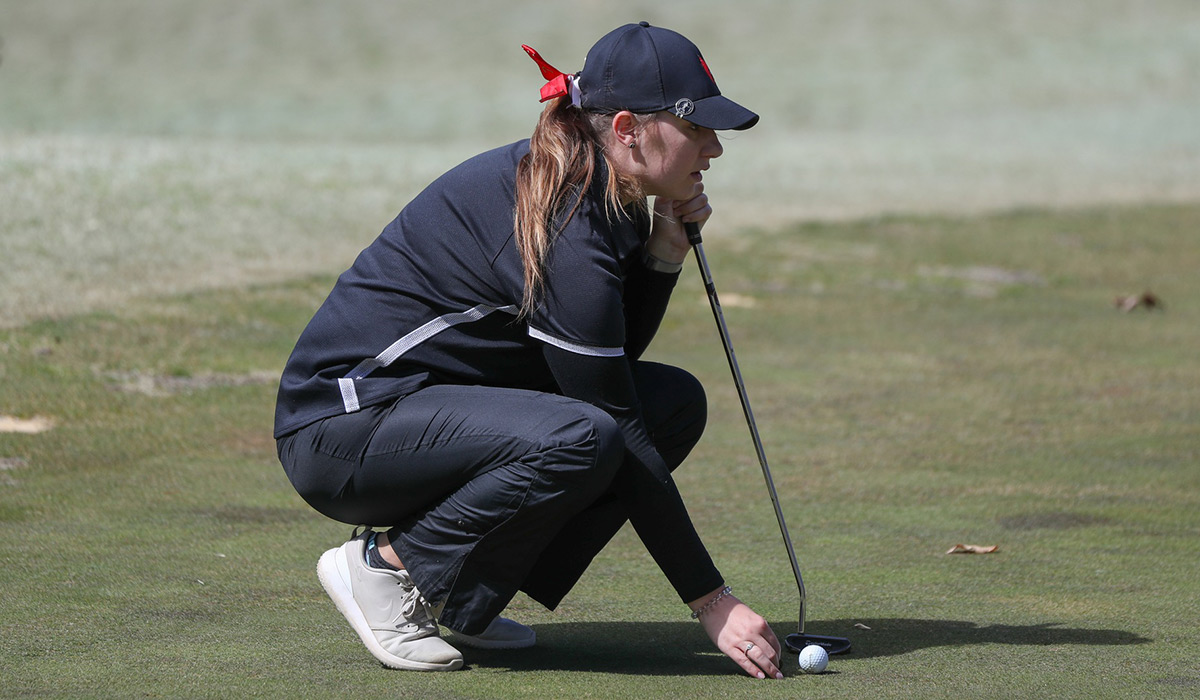 Female golf player squatting down to gauge distance to hole