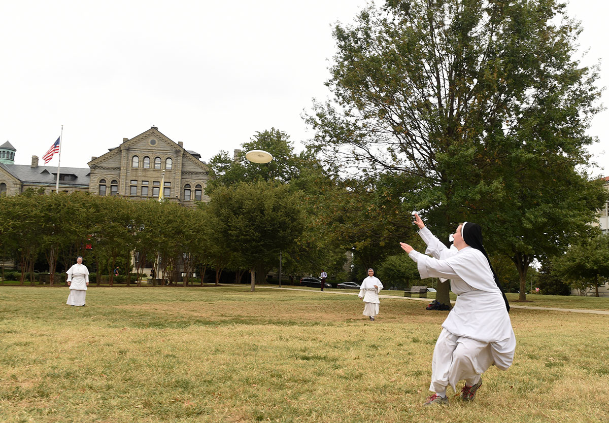 A group of religious sisters playing Frisbee on the lawn in front of McMahon Hall during lunchtime.