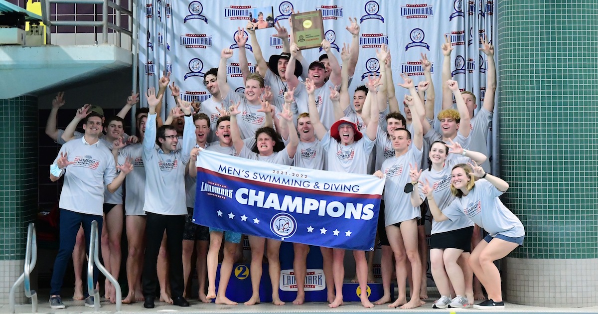 Members of CUA's men's swimming and diving team celebrate their victory as they pose with a banner saying they are the Landmark Conference champions.