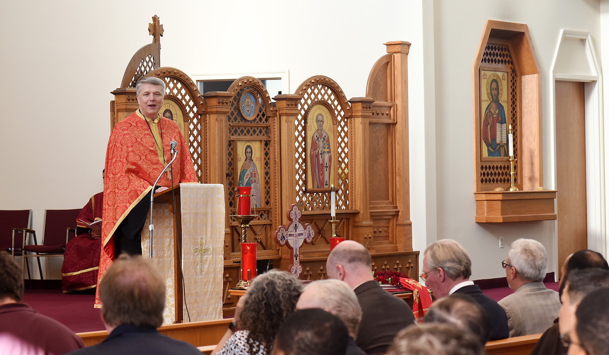 Dean Very Rev. Mark Morozowich S.E.O.D. speaks at a prayer service at the Ukrainian Catholic National Shrine of the Holy Family. He is wearing orange vestments. 