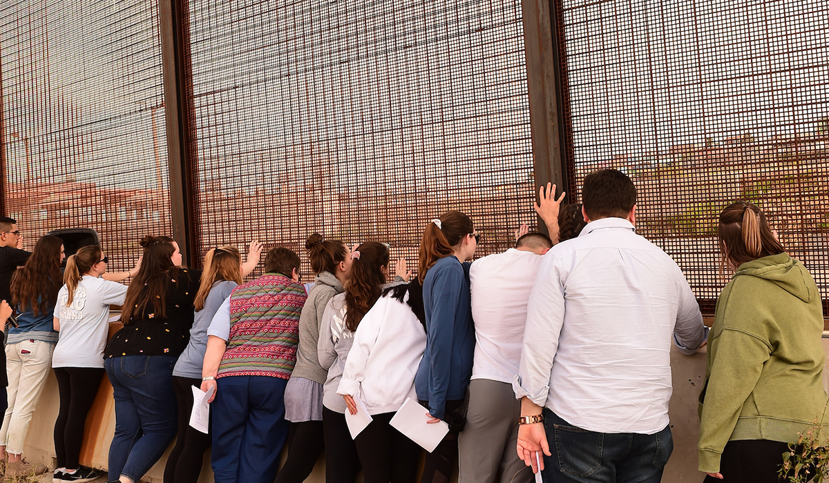 Students putting their hands on border fence